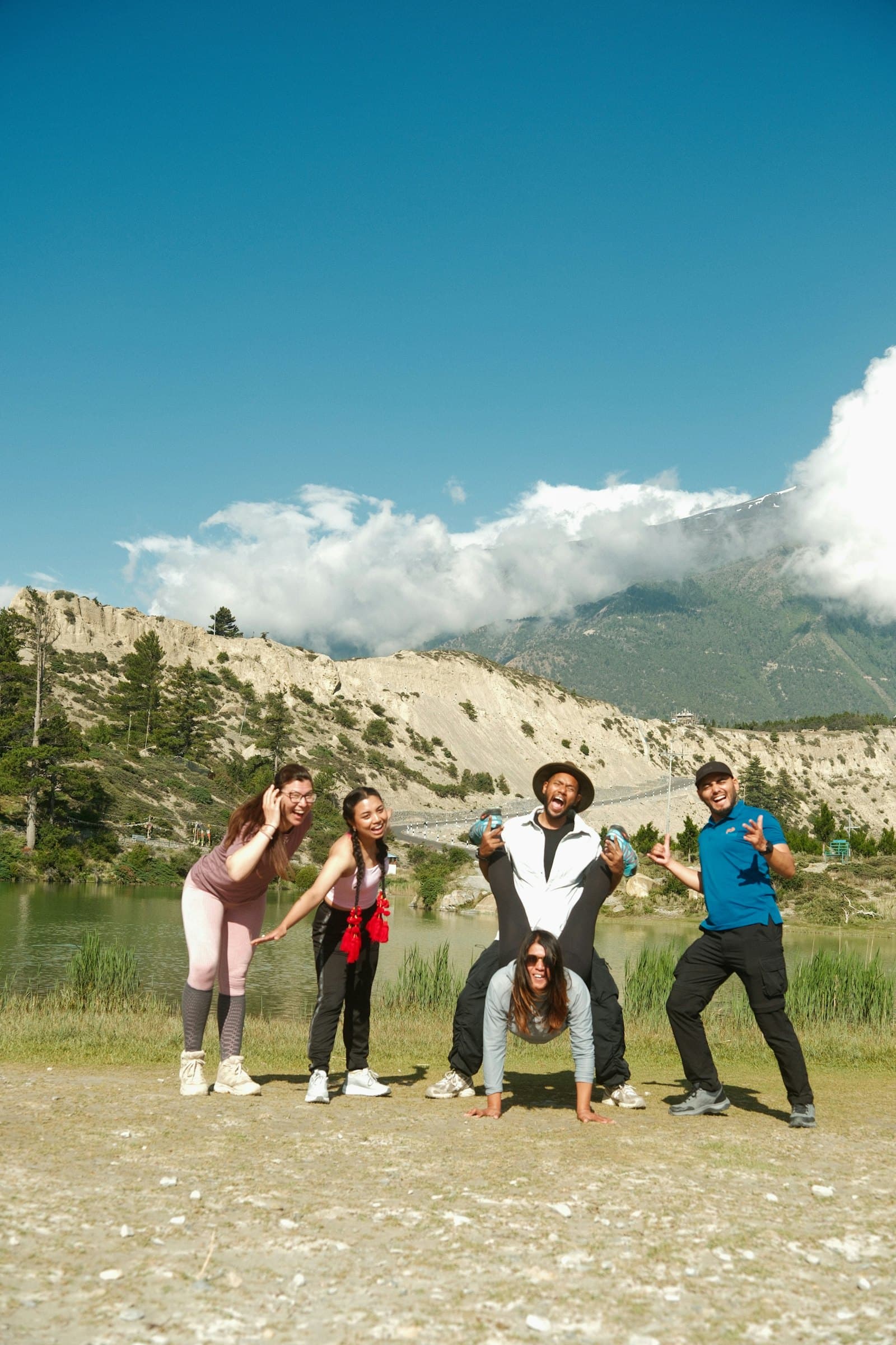 Cinco amigos posando divertidos frente a un lago y montañas